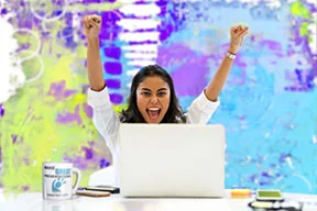 a woman with arms raised at laptop after creating a great and exciting presentation